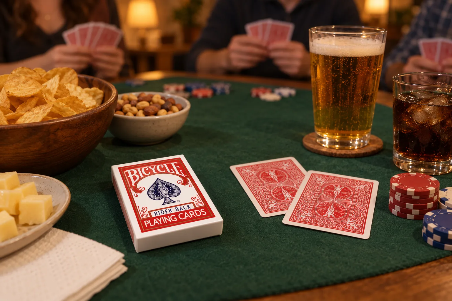 Patatine, frutta secca, formaggio e bevande accanto a un mazzo Bicycle Rider Back rosso e alle fiches in una partita di poker in casa