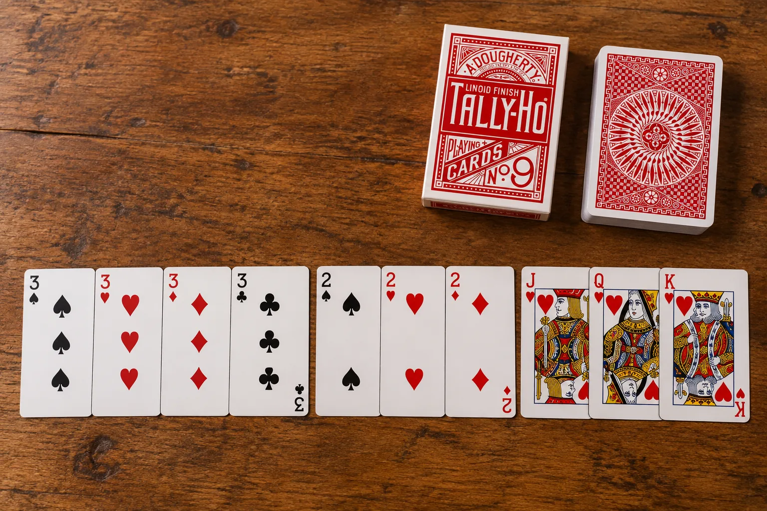 Mano de gin rummy de diez cartas totalmente combinada: cuatro treses, tres doses y la jota, la reina y el rey de corazones, junto a una baraja Tally-Ho Circle roja